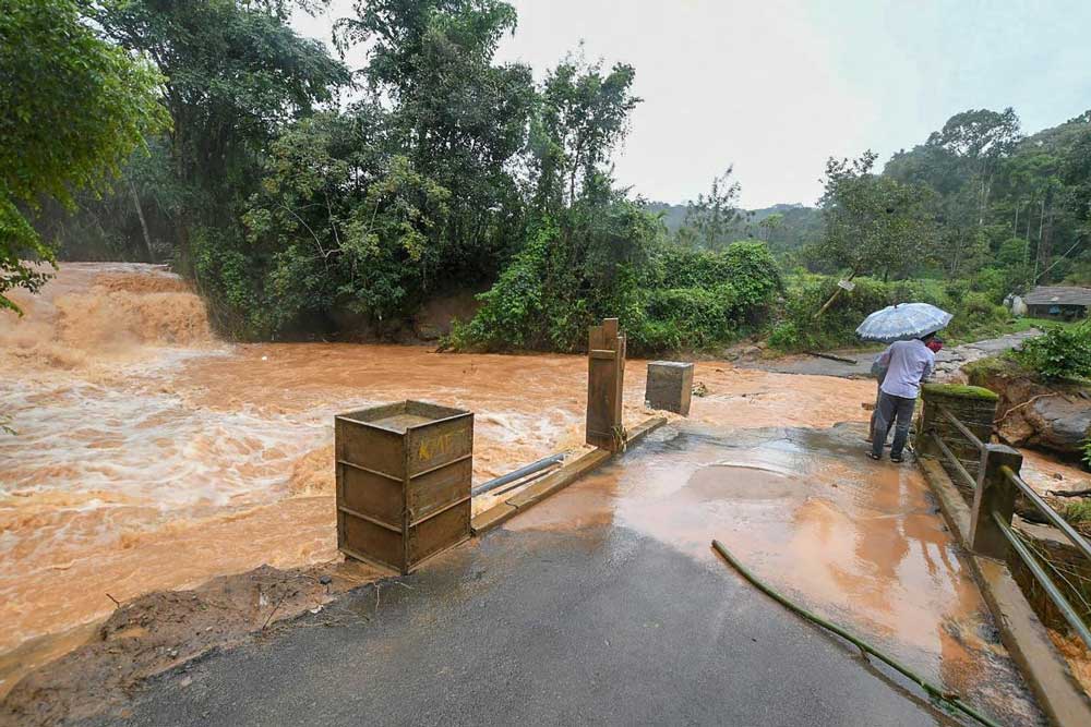 People walk across a bridge overflowing due to heavy monsoon rainfall, in Kodagu on Sunday. PTI Photo