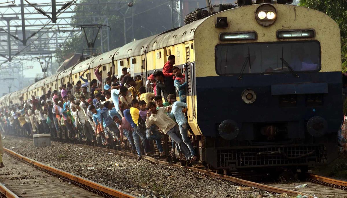 Passengers hang from the doors of the coaches of an over crowded train while traveling home for the Durga Puja festival in Patna. PTI