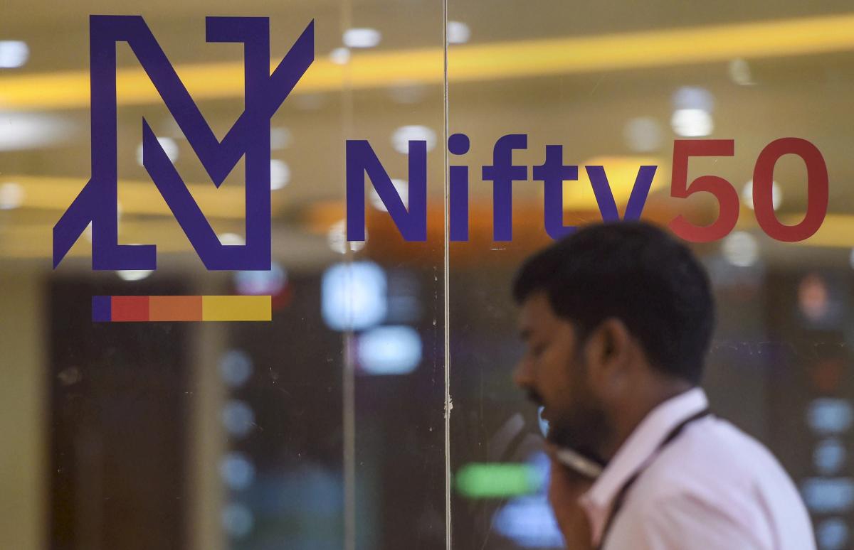 A man talks on phone at the National Stock Exchange as its new logo for for the benchmark Nifty50 is seen on a glass-wall, in Mumbai. PTI Photo
