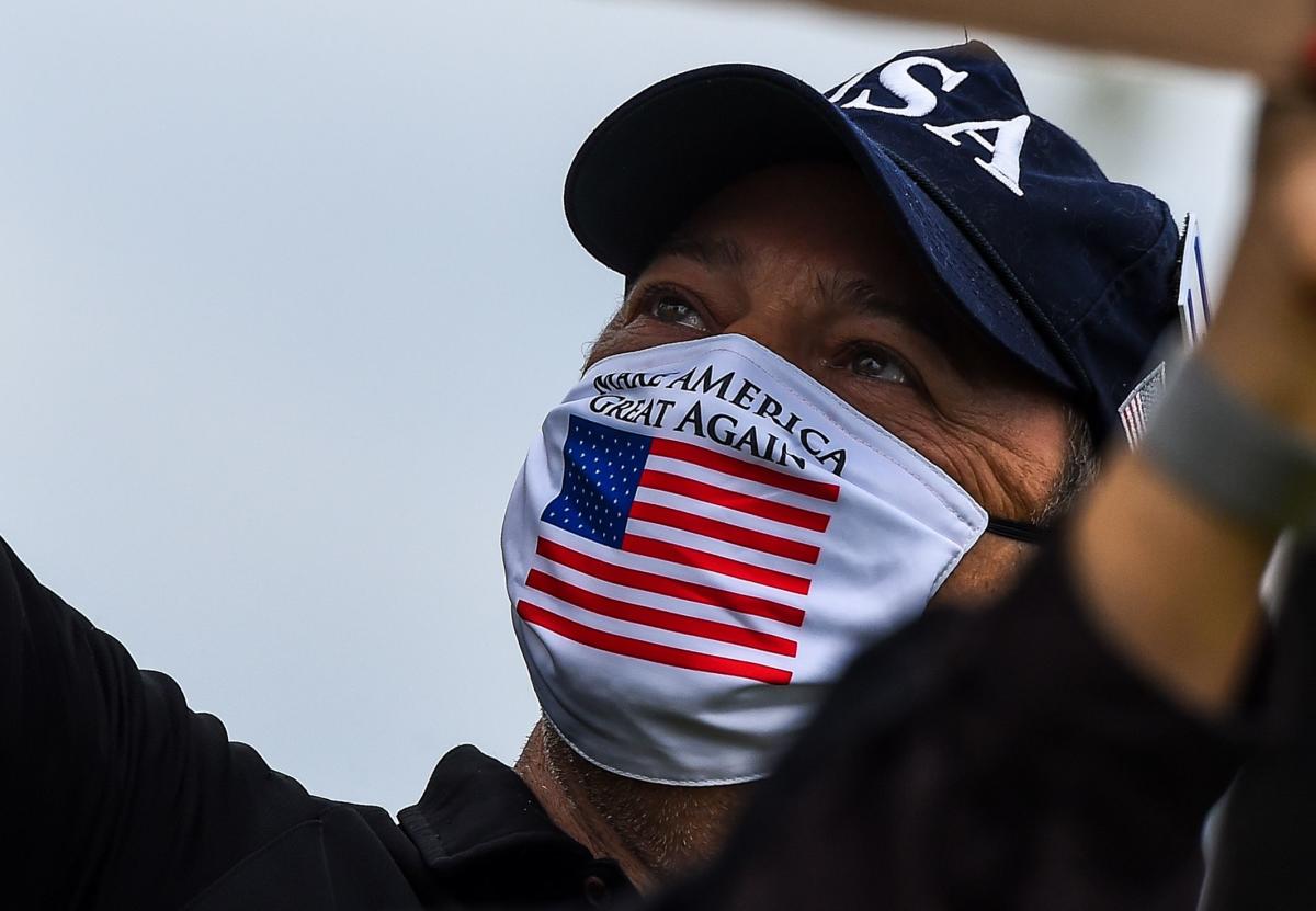 A supporter of US President Donald Trump wears a Trump mask as he participates in a