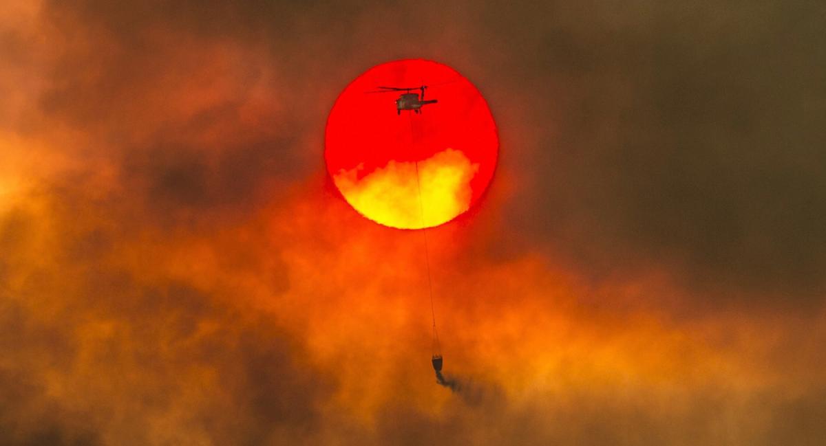 Redding : In this Friday, July 27, 2018 photo, a firefighting helicopter makes a water drop as the sun sets over a ridge burning near Redding, Calif., in efforts against the Carr Fire. Scorching heat, winds and dry conditions complicated firefighting efforts. AP/ PTI