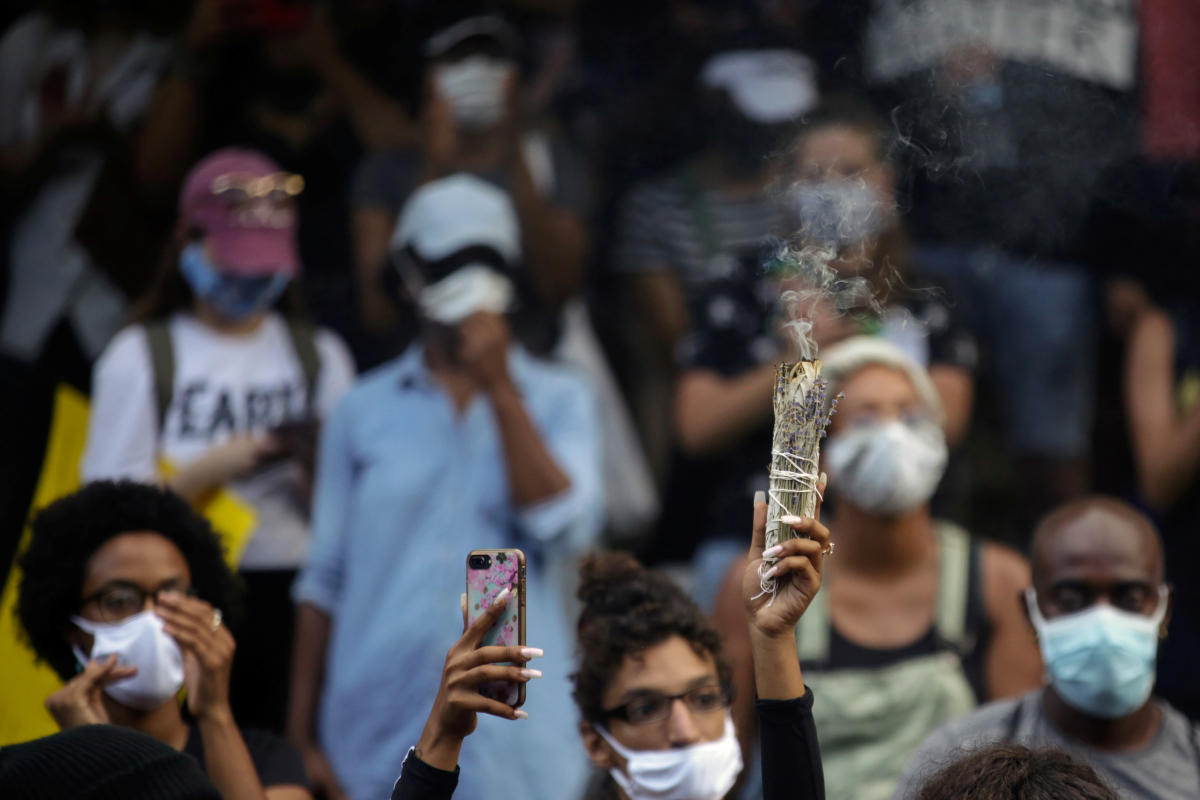 A woman raises burning sage in the air as she documents with her phone as protesters rally against the death in Minneapolis police custody of George Floyd, in New Orleans, Louisiana, U.S. May 30, 2020. REUTERS