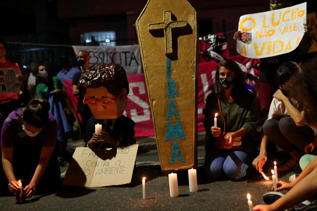 An activist wears a full head mask depicting Brazil's Environment Minister Ricardo Salles as people light candles during a protest calling for a