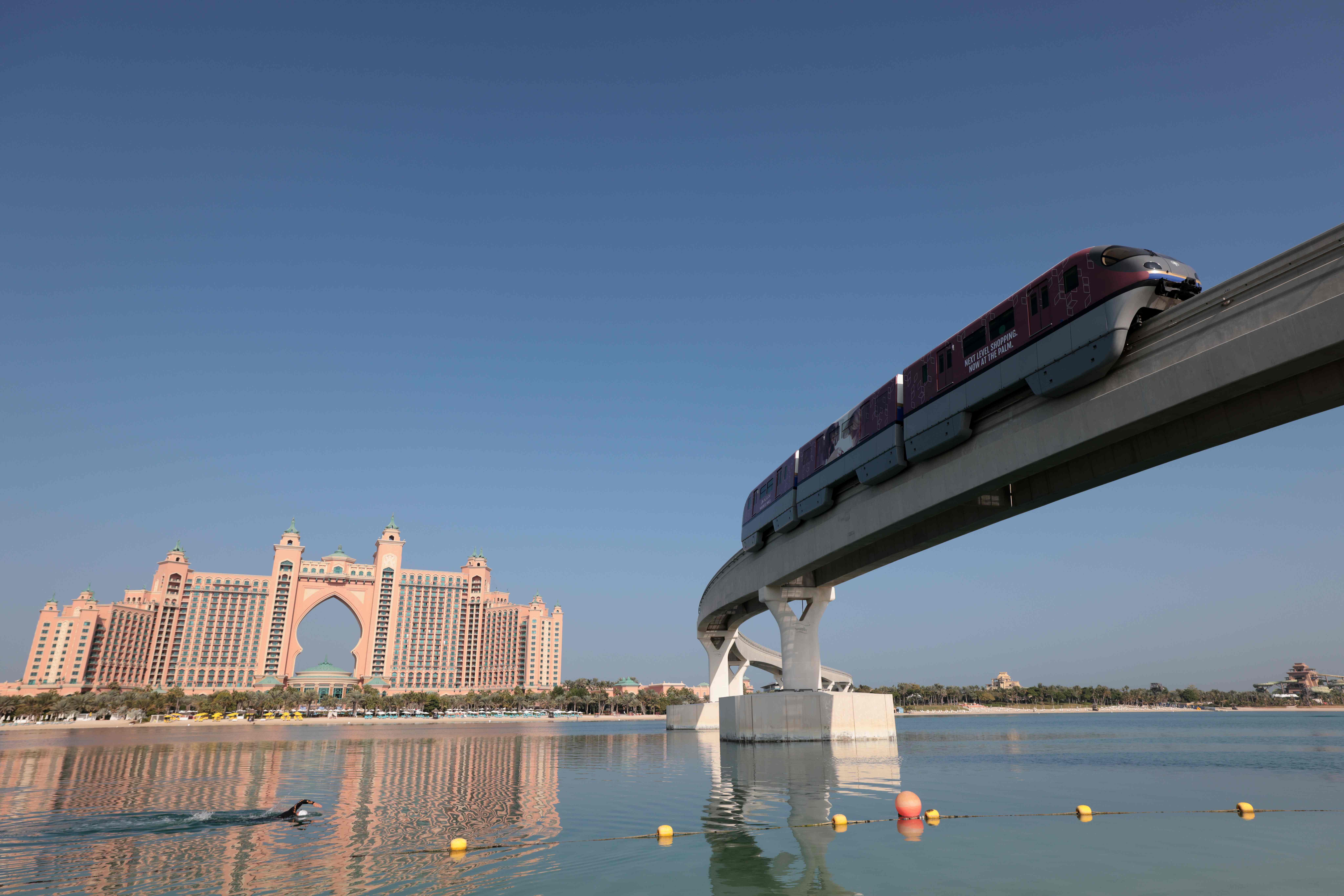 A man swims near a section of the Palm Jumeirah monorail in Dubai on November 16, 2020, backdropped by the Atlantis Hotel. Credit: AFP Photo