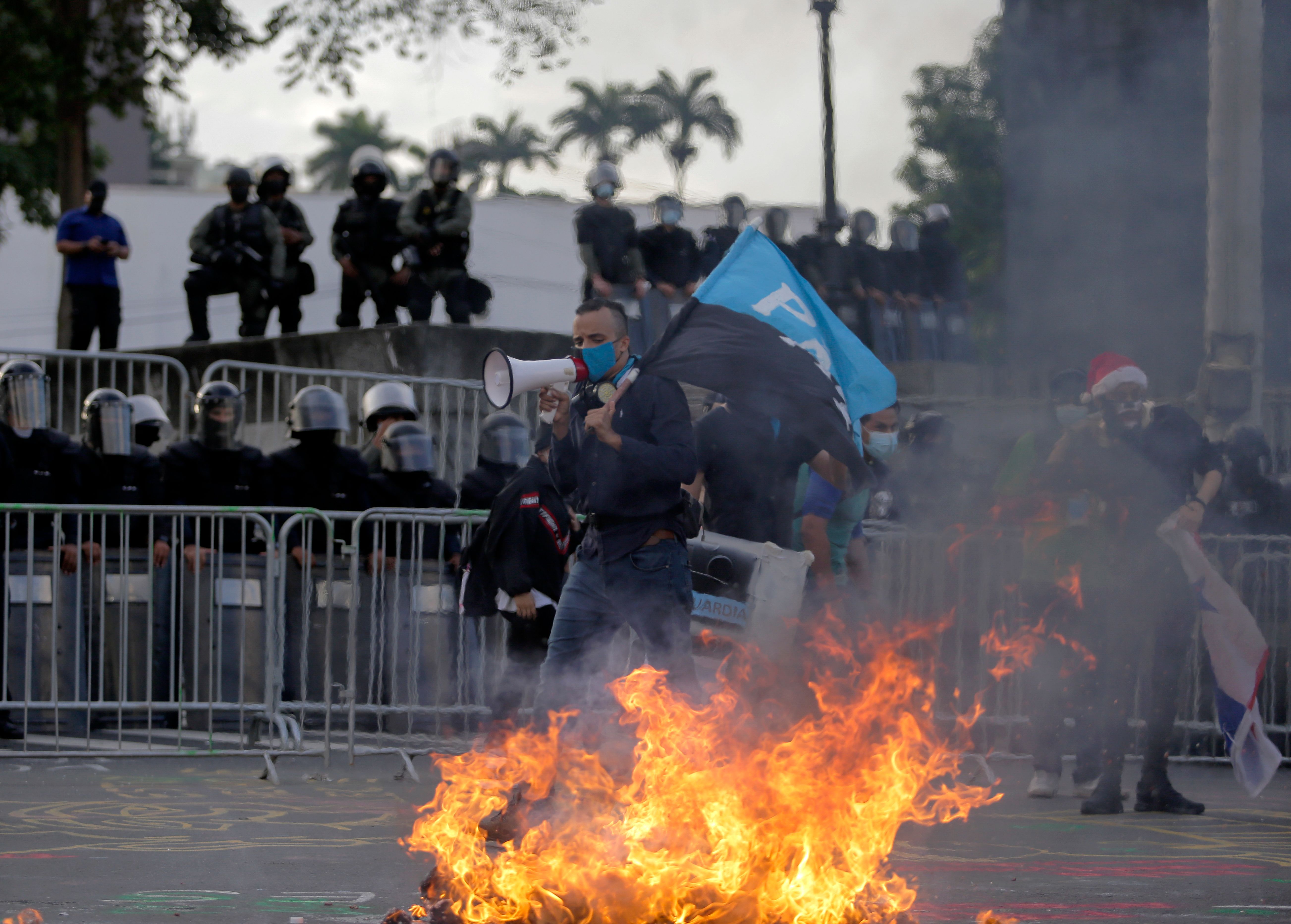 A man uses a megaphone next to a bonfire during a protest of youngsters as riot police stand guard outside the National Assembly building in Panama City. Credit: AFP