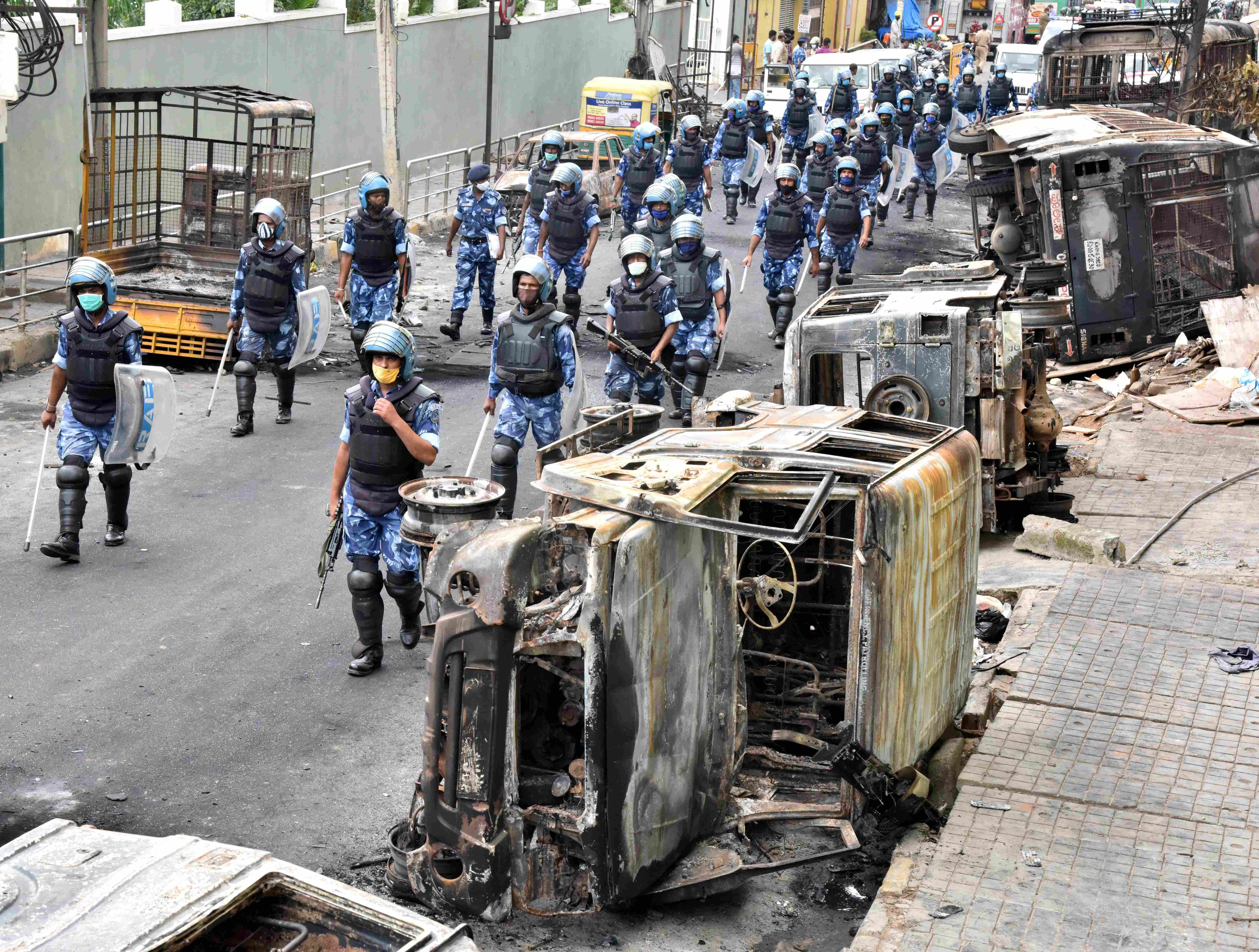 DJ Halli and KG Halli riots mar Bengaluru | RAF and CISF personnel march after a mob attacked and burnt vehicles in front of DJ Halli Police Station, in Bengaluru. Three people were killed after police opened fire on August 11 night to quell a mob that went on a rampage over an inflammatory social media post allegedly put out by P Naveen, a relative of Pulakeshinagar Congress MLA R Akhanda Srinivasa Murthy. The MLA's residence and a police station at D J Halli were torched by the rioters, who also set ablaze many police and private vehicles, besides looting the belongings of the legislator and his sister. More than 300 people have been arrested in connection with the violence.  Credit: DH Photo/  Janardhan BK