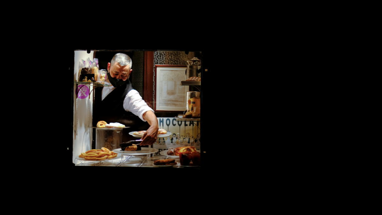 A waiter, wearing a protective face mask, picks up a sweet takeaway at a bakery in the Gothic Quartier, after Catalonia's government imposed new restrictions in an effort to control the spread of Covid-19 in Barcelona. Credit: Reuters Photo