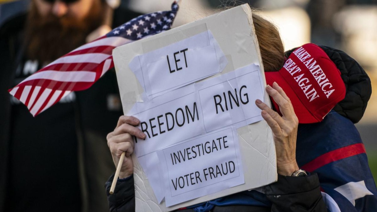 A supporter of President Donald Trump holds a MAGA hat and sign reading