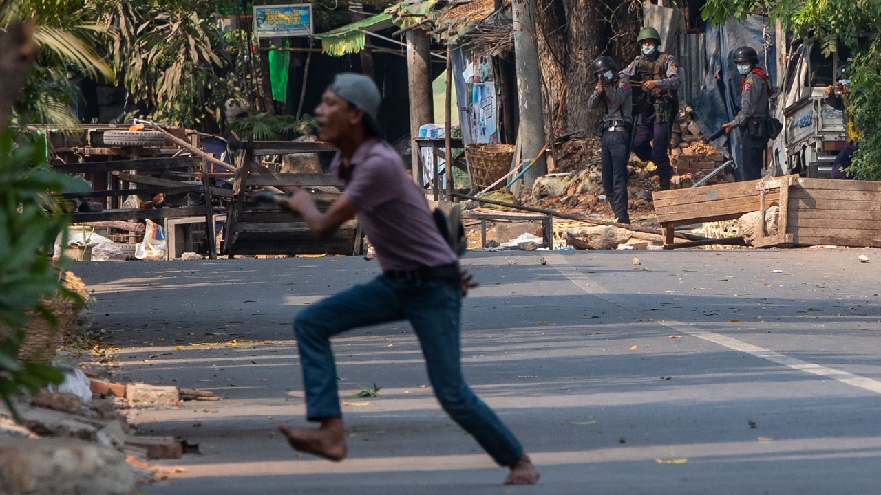 A protester runs as a security force (top L) aims a gun during a demonstration against the military coup in Mandalay. Credit: AFP Photo