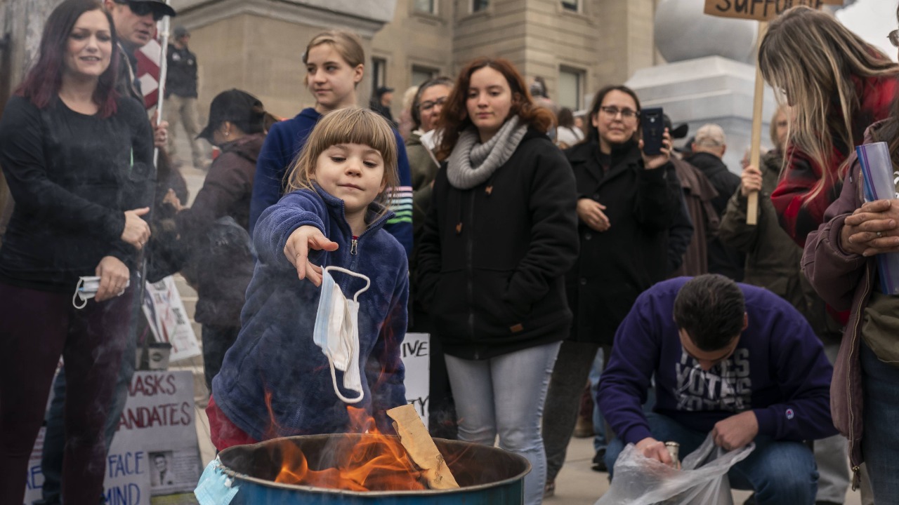 A child tosses a surgical mask into a fire during a mask burning event at the Idaho Statehouse. Credit: AFP Photo