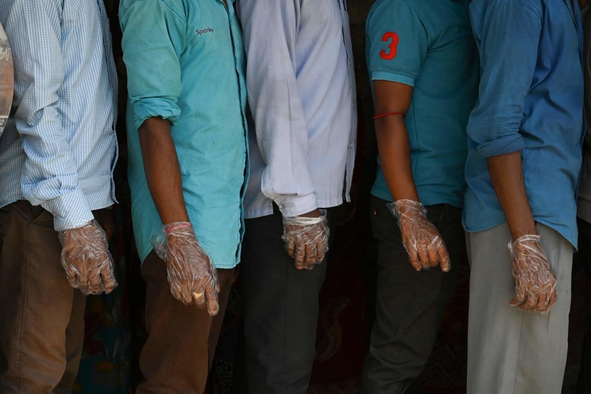 Voters wearing plastic gloves stand in a line to cast their vote outside a polling station during Phase 2 of West Bengal's legislative election in Nandigram. Credit: AFP Photo