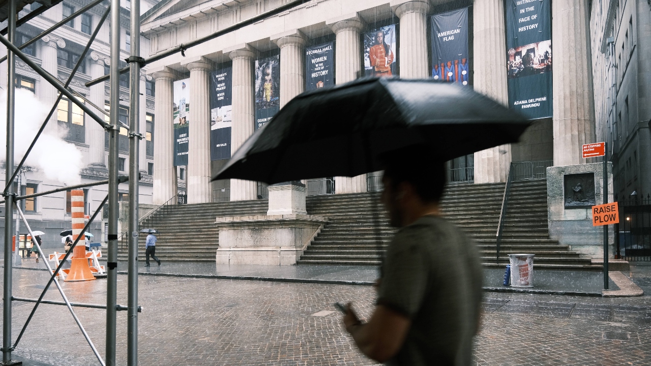 People walk along Wall Street in the rain in New York City. Credit: AFP Photo