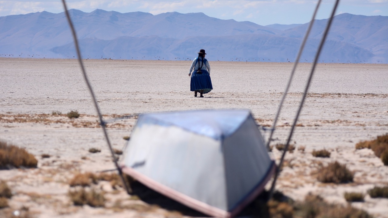 Cristina Mamani walks near an unused boat in Lake Poopo, Bolivia's second largest lake which has dried up due to water diversion for regional irrigation needs and a warmer, drier climate, according to local residents and scientists, in Lake Poopo, Bolivia. Credit: Reuters Photo