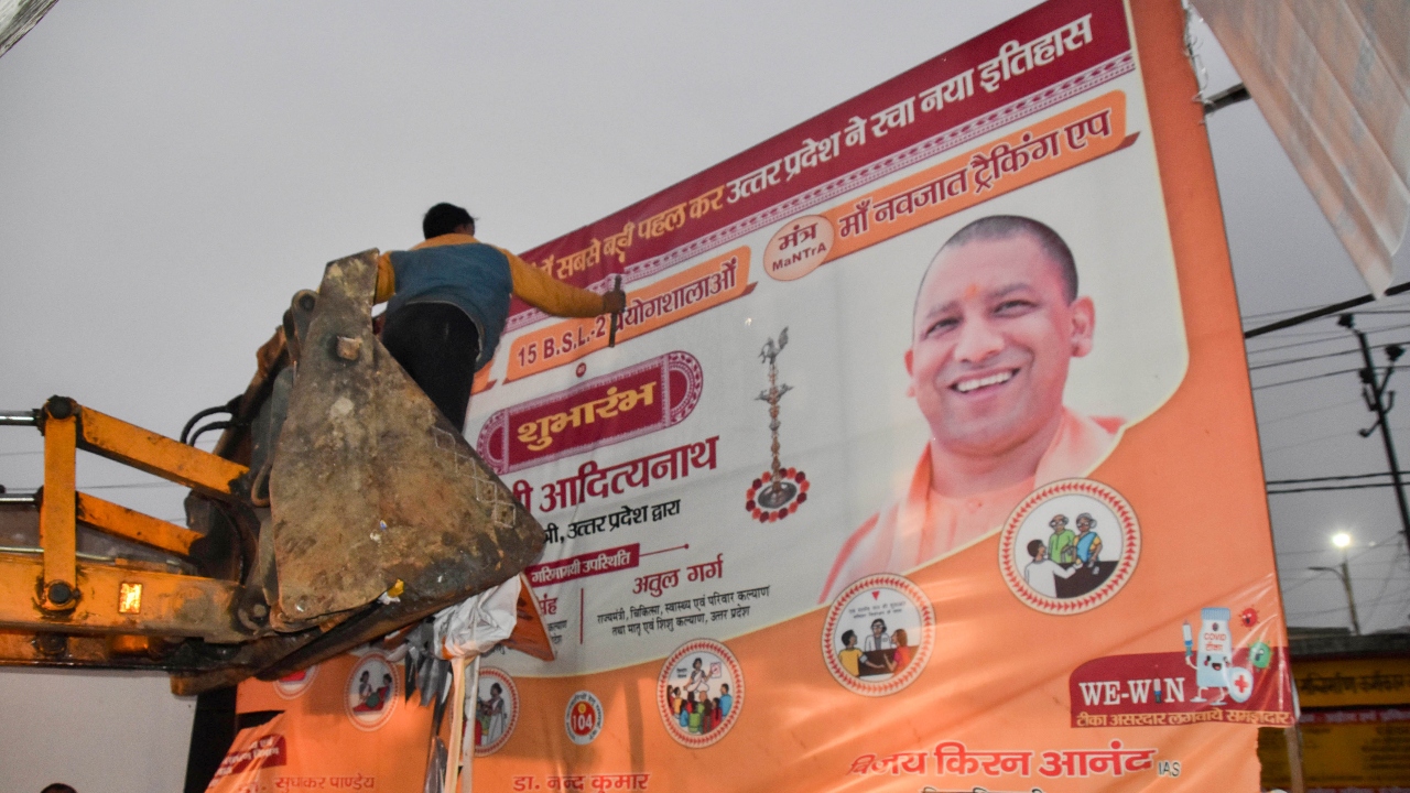 A worker is seen removing a banner as the Model Code of Conduct has come into effect after the announcement of the schedule of UP Assembly elections, in Lucknow. Credit: PTI Photo