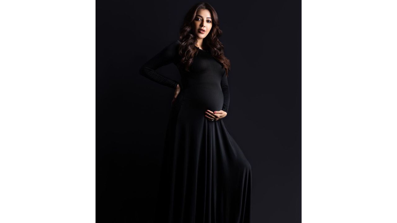 Kajal cradles her baby bump as she poses in a black pleated dress for a photoshoot. Credit: Instagram/kajalaggarwalofficial