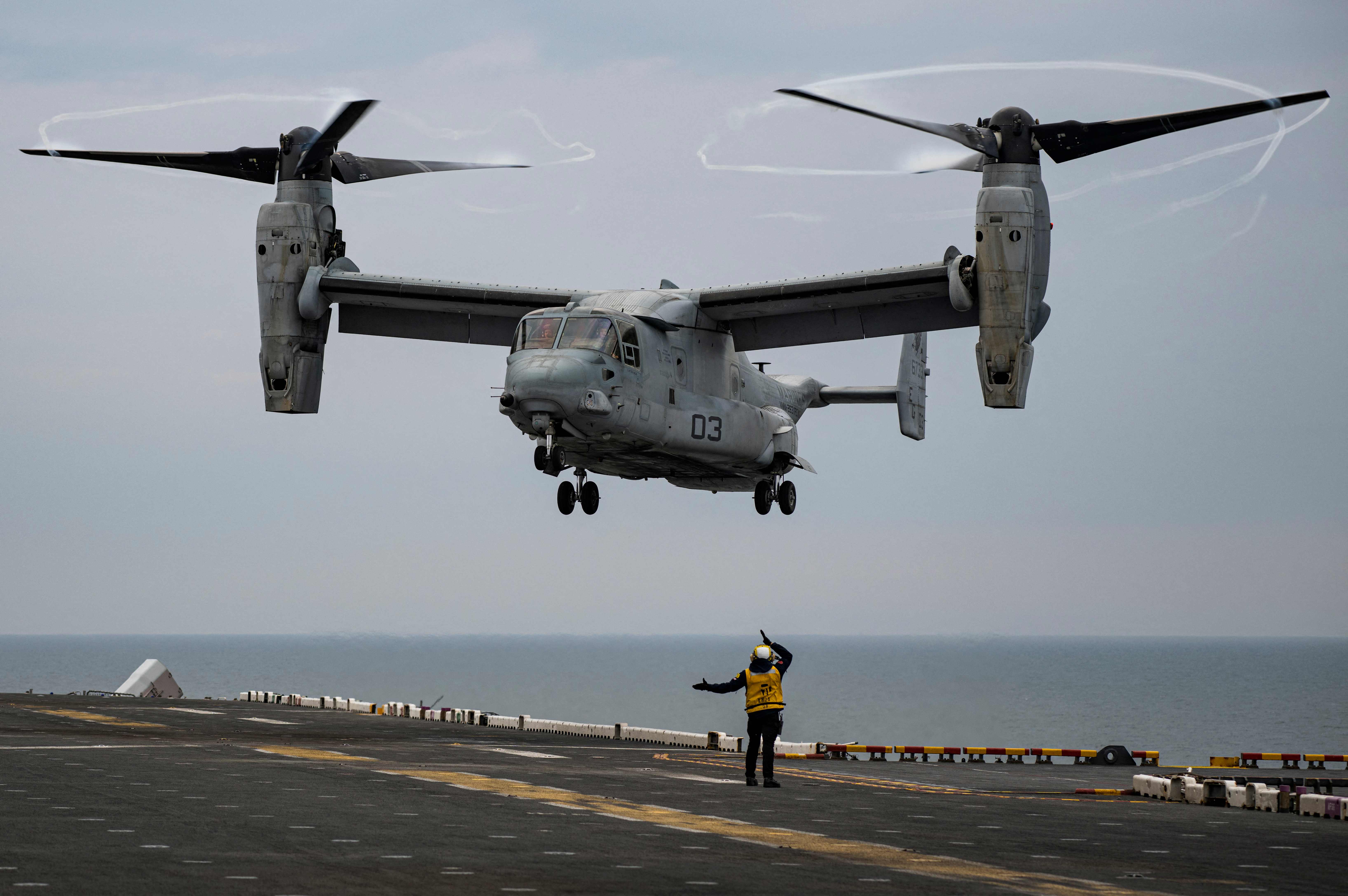 An Aviation Boatswain’s Mate (Bottom) signals to the pilots of the MV-22 Osprey assault support aircraft, assigned to the 22nd Marine Expeditionary Unit. Credit: AFP Photo