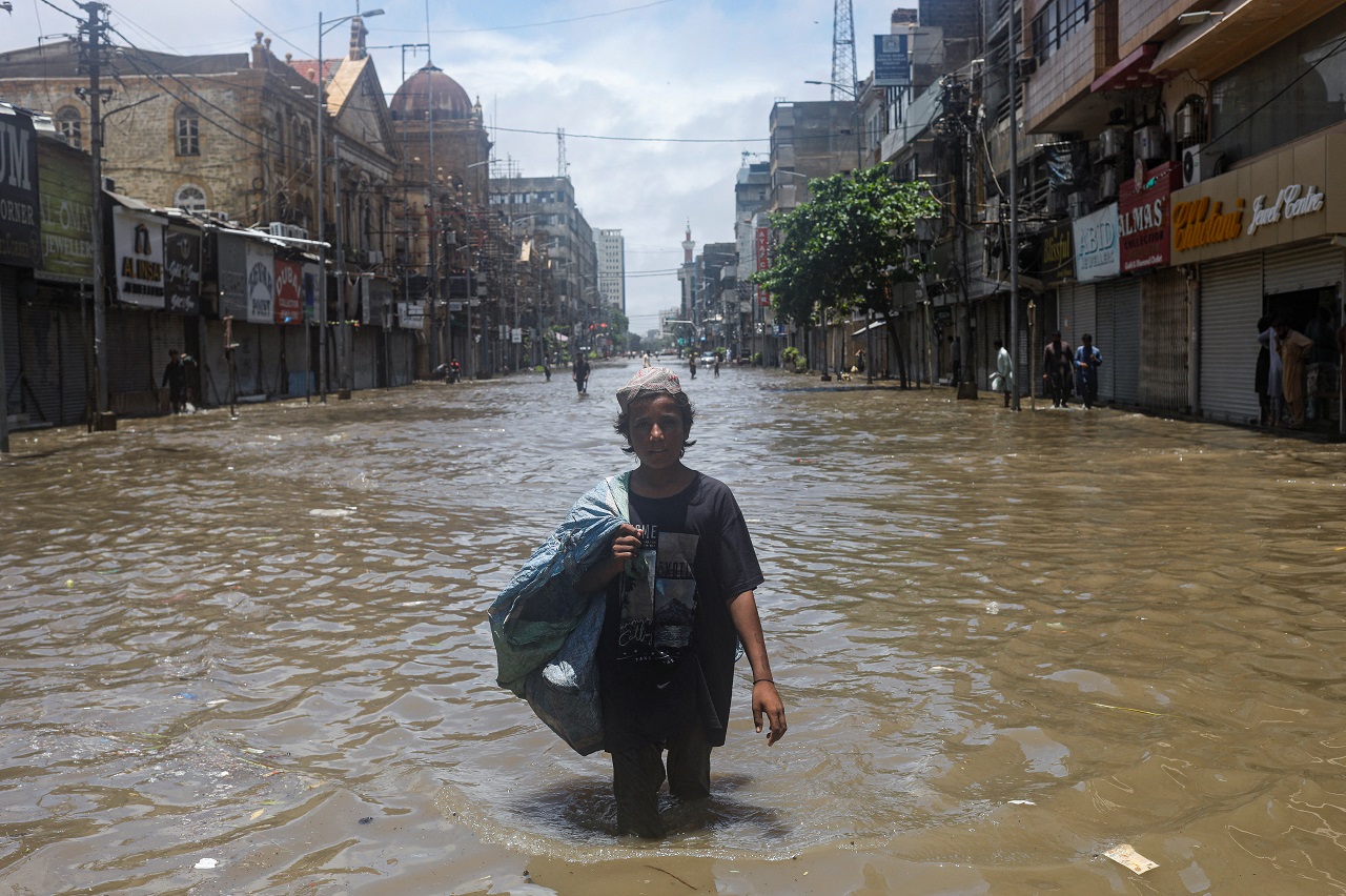 Qudratullah, 15, whose family moved to Karachi from Afghanistan to look for work, carries a bag of recyclables while wading through a flooded street during the monsoon season in Karachi. Credit: Reuters Photo