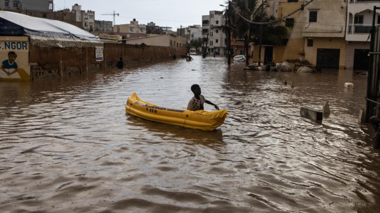 A young boy pushes his inflatable canoe down a flooded road after heavy rains in Dakar on August 5, 2022. Credit: AFP Photo