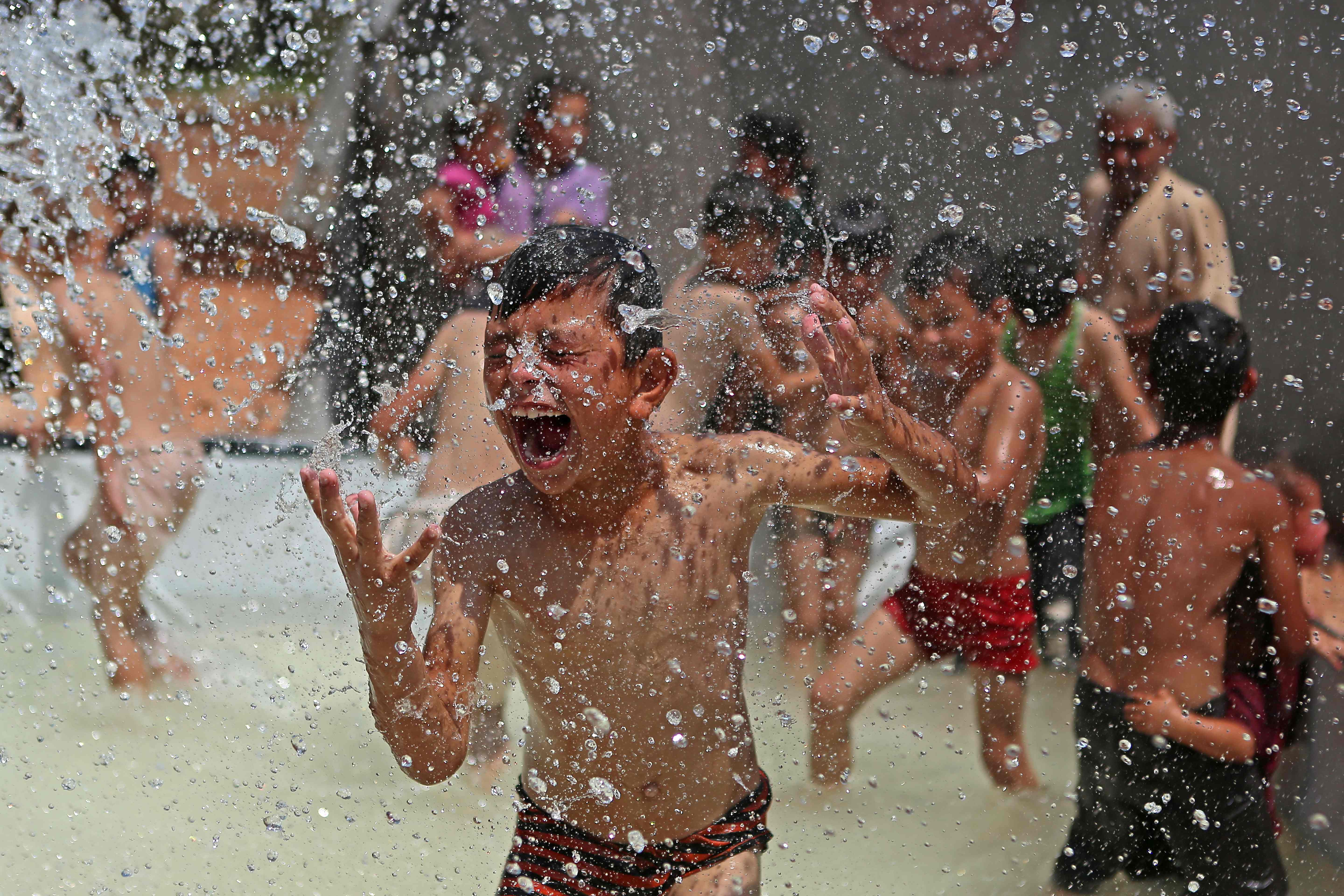 A Syrian boy reacts as he gets sprayed with water in a portable swimming pool set up by volunteers, at a camp for the displaced in the rebel-held town of Kafr Yahmul in the northern countryside of Idlib. Credit: AFP Photo