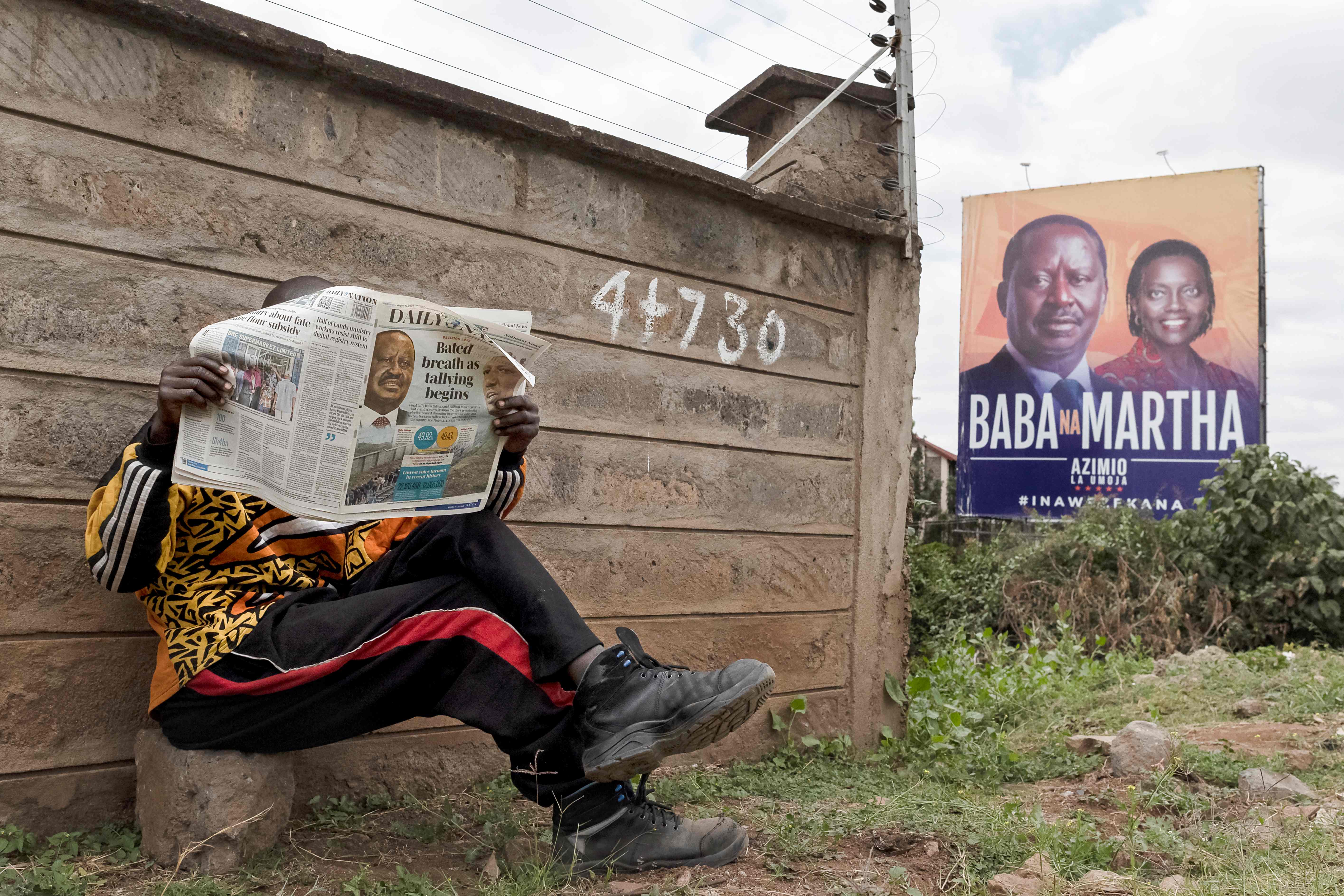 A man reads the Daily Nation newspaper while seated near a campaign billboard of Azimio la Umoja political coalition presidential flag bearer Raila Odinga and his running mate Martha Karua, following Kenya's general election in Nairobi. Credit: AFP Photo