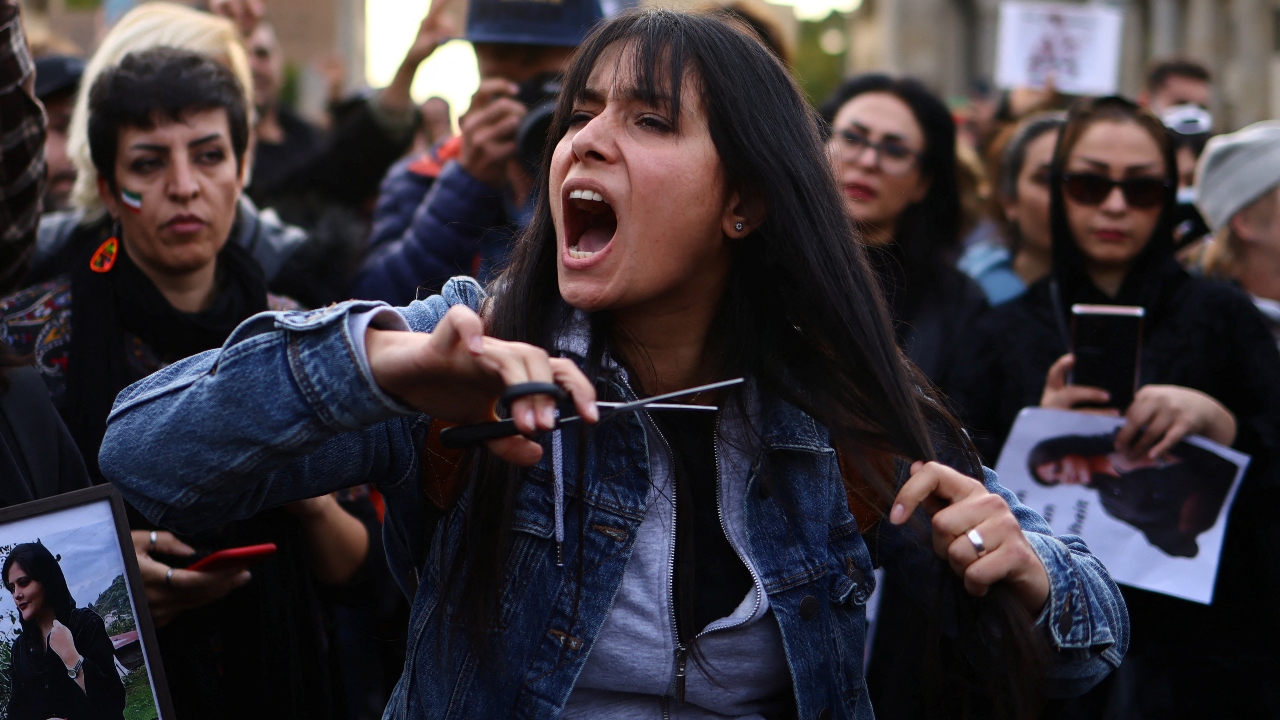 A demonstrator cuts hair during a protest following the death of Mahsa Amini, in front of the Brandenburg Gate in Berlin, Germany. Credit: Reuters Photo
