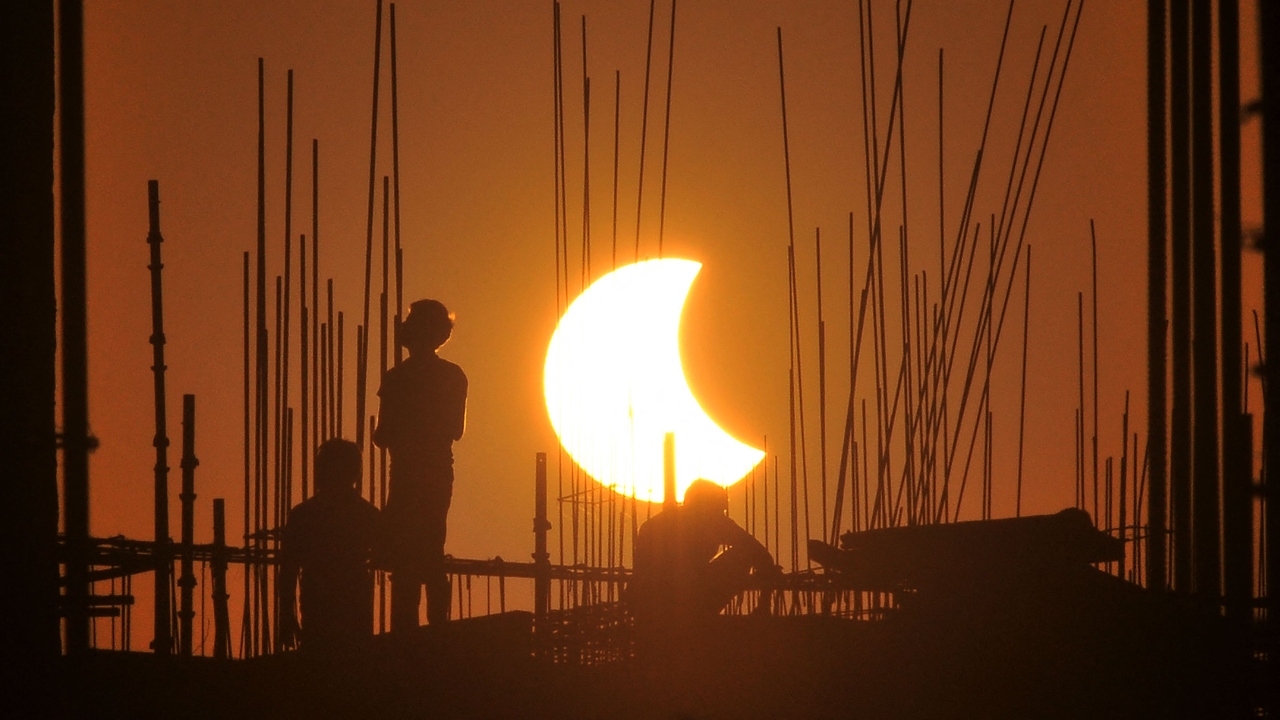Labourers work at a construction site as the moon partially obscures the sun during the partial solar eclipse visible from Gurgaon. Credit: AFP Photo