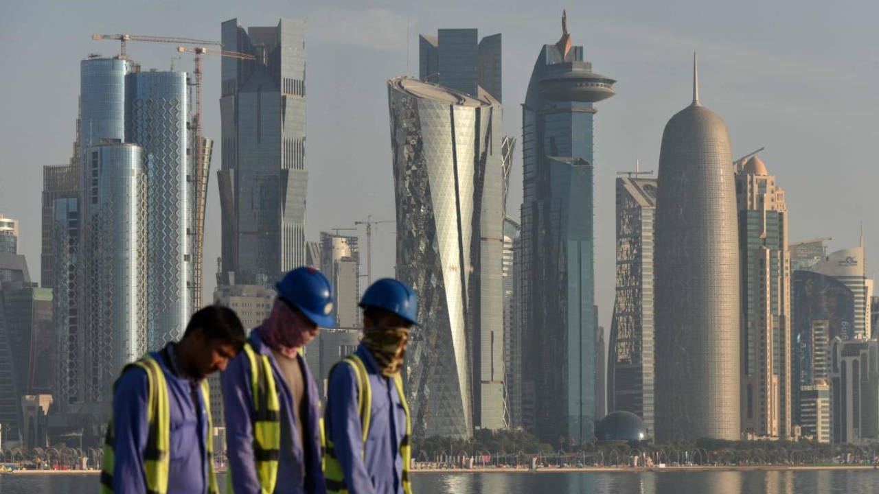 Workers are backdropped by the skyline of Doha as they walk along the Corniche seafront promenade in Doha early morning on November 17, 2022, ahead of the Qatar 2022 World Cup football tournament. Credit: AFP Photo