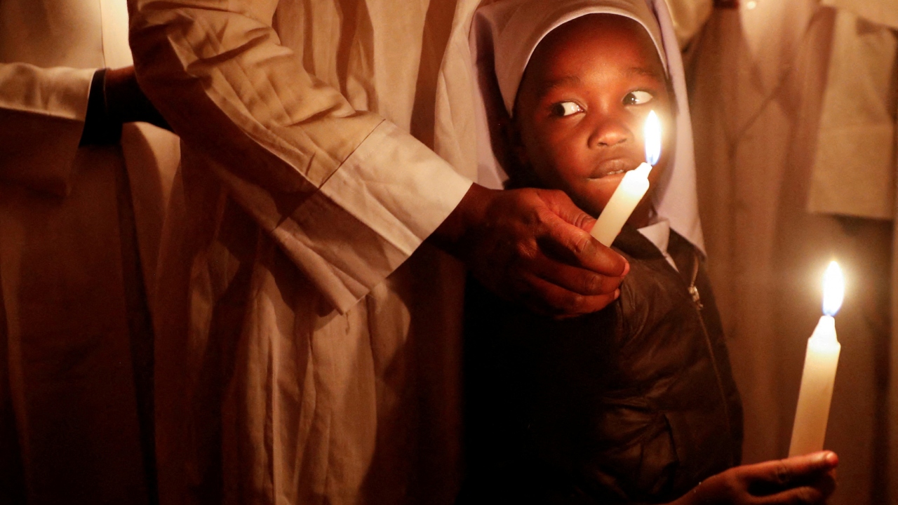 A worshiper guides her child after lighting a candle during Easter vigil prayers at the St. Joanes, Legio Maria of African Church Mission within Fort Jesus in Kibera district of Nairobi, Kenya. Credit: Reuters Photo