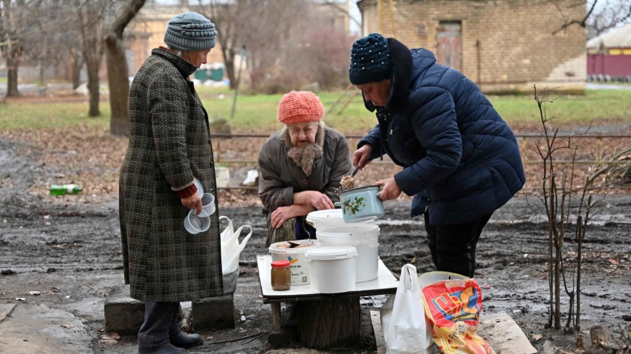 A local resident distributes to her neighbours hot food brought by volunteers in the yard of a residential building in the de-occupied town of Izyum, Kharkiv region on December 22, 2022, amid the Russian invasion of Ukraine. Credit: AFP Photo