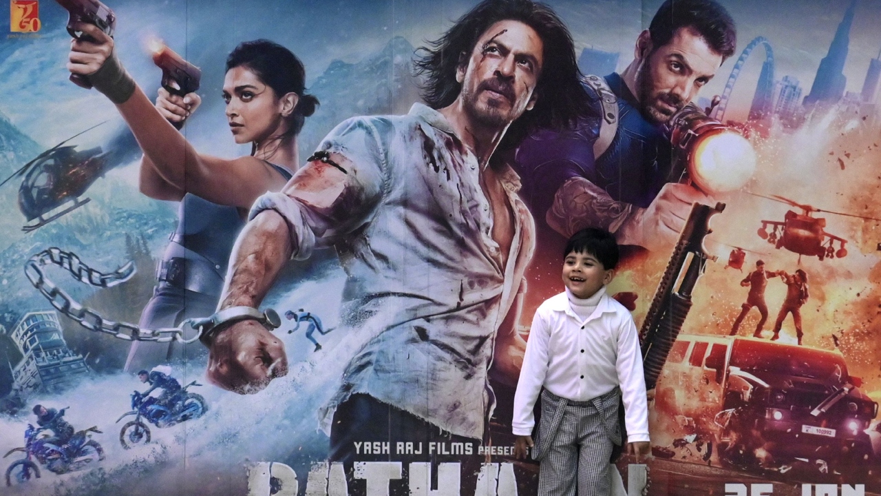 A young SRK fan poses in front of a poster of the Bollywood movie 'Pathaan' outside a cinema hall in Prayagraj. Credit: AFP Photo