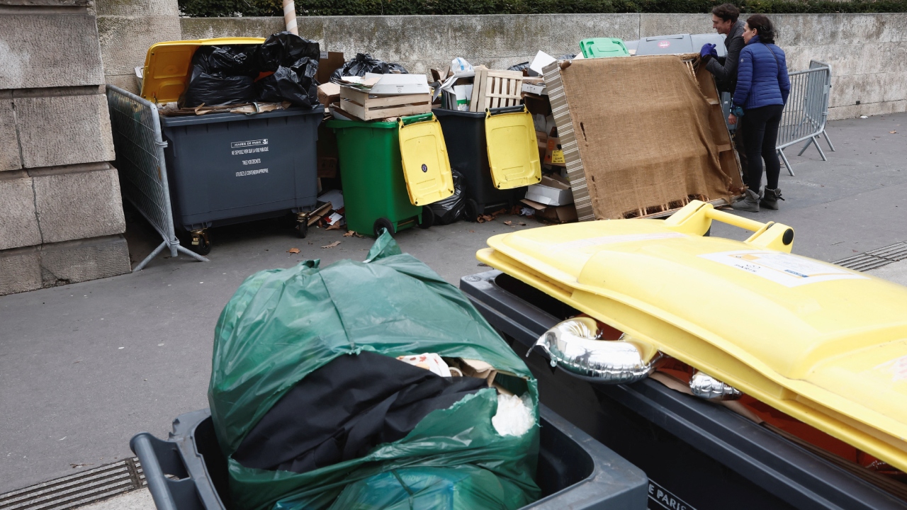 People stand on a street where trash is overflowing, Paris. This is a critical time for both sides (protesting unions and the government) since the government is hoping the pension changes will be adopted by parliament by the end of the month. Credit: Reuters Photo