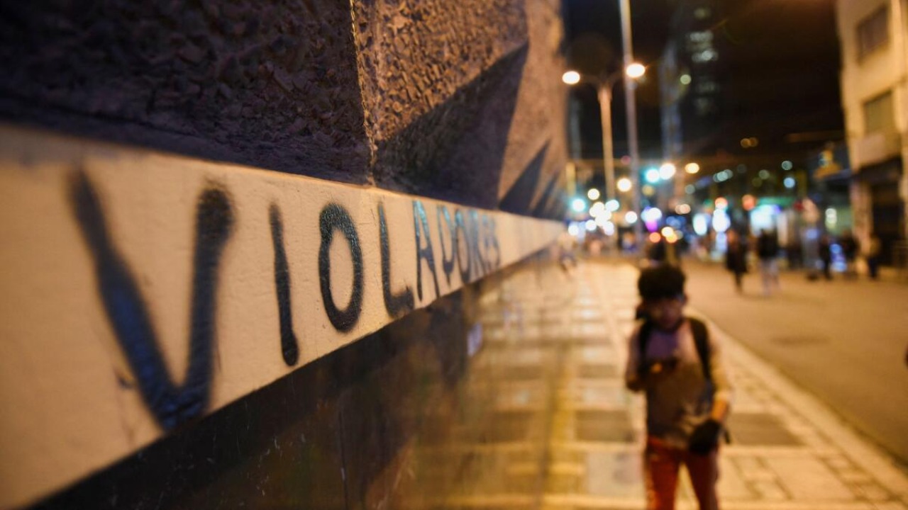 A person walks next to a wall with a gaffiti that reads