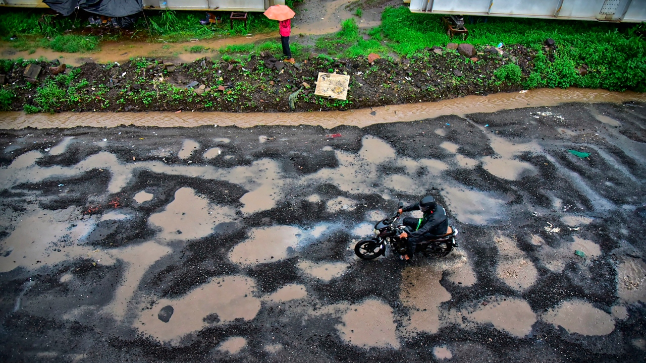 A commuter rides through a pothole-ridden road in Juinagar after monsoon rainfall in Navi Mumbai. Credit: PTI Photo