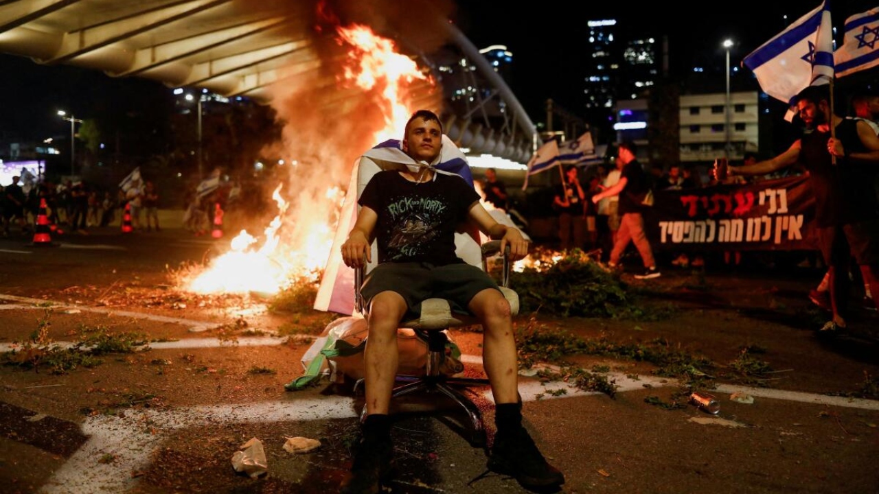 A protester sits as fire emerges during a demonstration against Israeli Prime Minister Benjamin Netanyahu and his nationalist coalition government's judicial overhaul, in Tel Aviv, Israel July 20, 2023. Credit: Reuters Photo