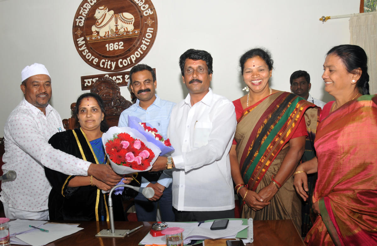 Corporator SBM Manju, who was elected as a representative to Mysuru Urban Development Authority, being greeted by Mayor Pushpalatha Jagannath and Deputy Mayor Shafi Ahmad, during the council meeting of the Mysuru City Corporation, on Thursday. MCC Commiss