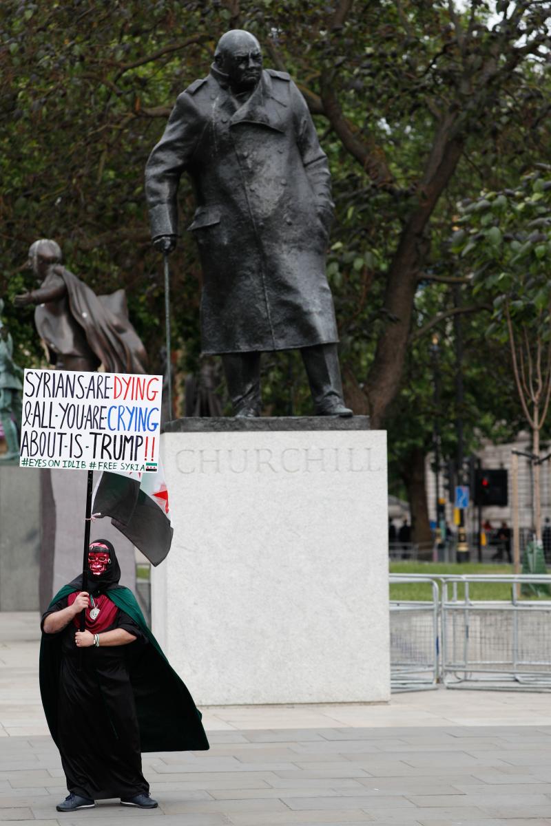 A protester holds a protest placard regarding the conflict in Syria in front of the statue of Winston Churchill outside the Houses of Parliament where demonstrators are gathering for an anti-Trump demonstration in London on June 4, 2019, on the second day