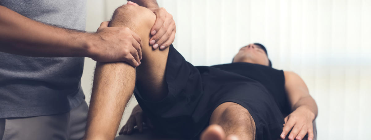Therapist treating injured knee of athlete male patient - sport physical therapy concept, panoramic bannerSports Physician 