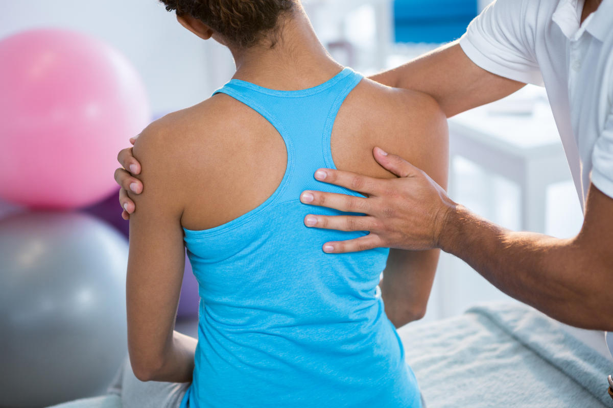 Physiotherapist giving back massage to female patient in clinicSports Physician 