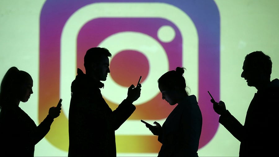 <div class="paragraphs"><p>Silhouettes of mobile users are seen next to a screen projection of Instagram logo.</p></div>
