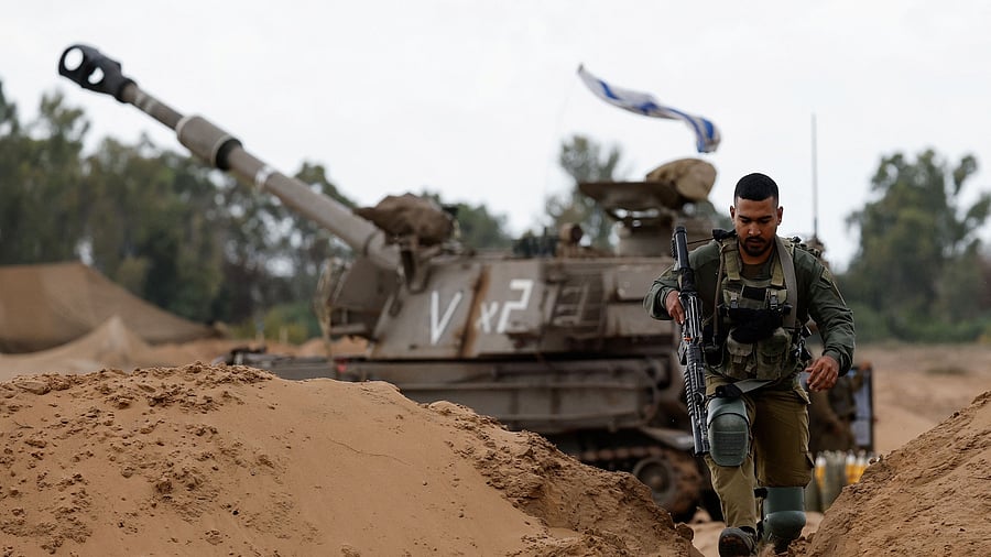 <div class="paragraphs"><p>An Israeli soldier walks by a mobile artillery unit, amid the ongoing conflict between Israel and the Palestinian Islamist group Hamas, near the northern Gaza border, in southern Israel.</p></div>