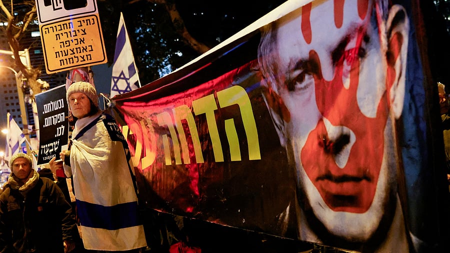 <div class="paragraphs"><p>A demonstrator stands next to a banner with an image of Israeli Prime Minister Benjamin Netanyahu.</p></div>