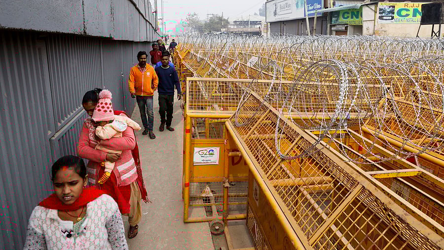 <div class="paragraphs"><p>People walk by barricades as police officers and workers erect them on a national highway to stop farmers, who are marching towards New Delhi to press for the better crop prices promised to them in 2021, at the Singhu border in New Delhi, India, February 13, 2024. </p></div>