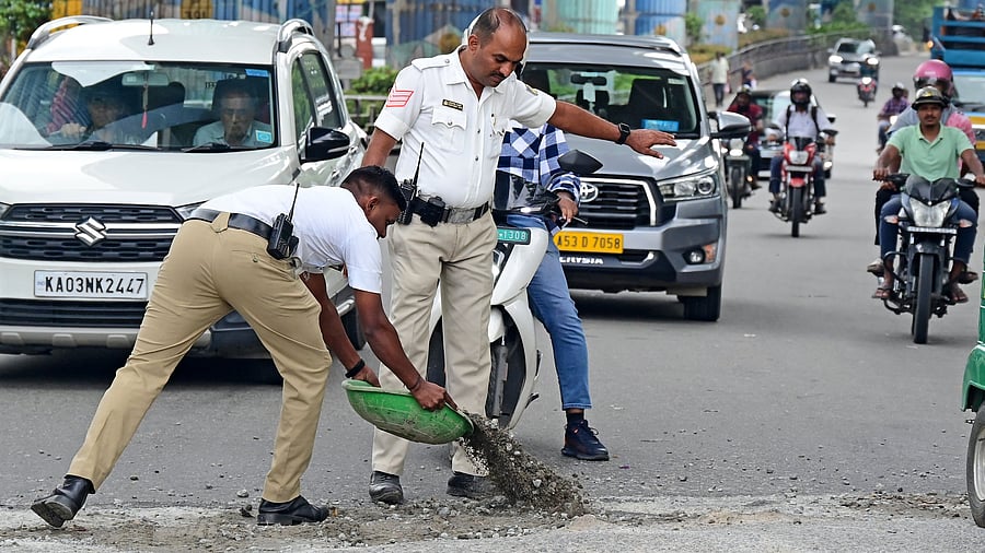 <div class="paragraphs"><p>Traffic policemen fill a pothole at Kimco Junction in Deepanjali Nagar, Mysuru Road. Potholes turn into ponds after a heavy&nbsp;downpour, affecting vehicular movement. </p></div>