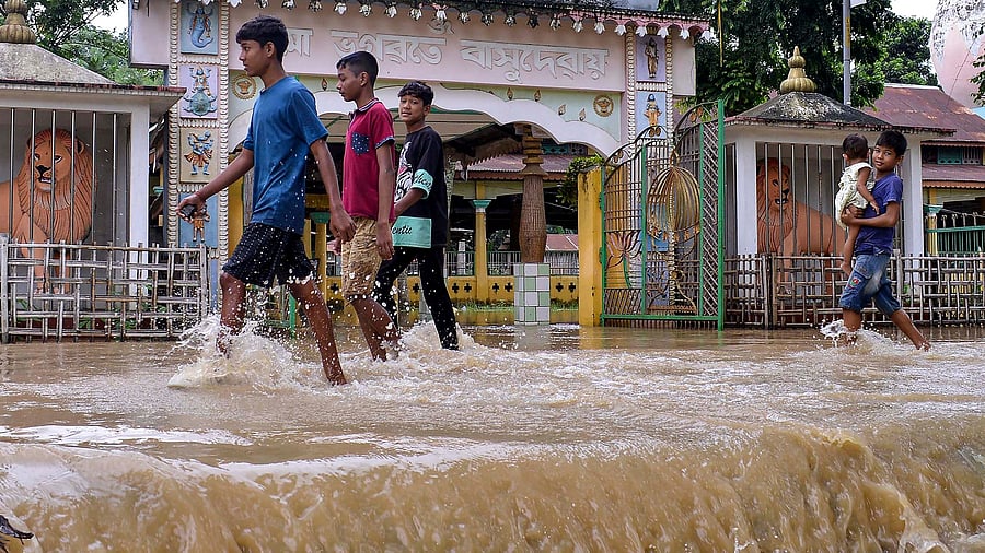 <div class="paragraphs"><p>People walk through a flooded area following rains in Assam.</p></div>