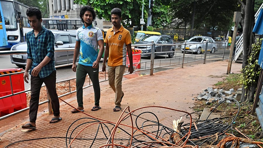 <div class="paragraphs"><p>Pedestrians walk past bundled optical fibre cables occupying the footpath near the Halasuru Gate traffic police station.</p></div>