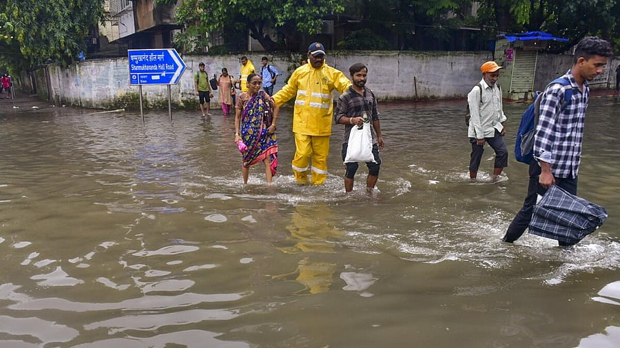 <div class="paragraphs"><p>Disaster response force personnel help pedestrians to cross a waterlogged street following rains, in Mumbai</p></div>