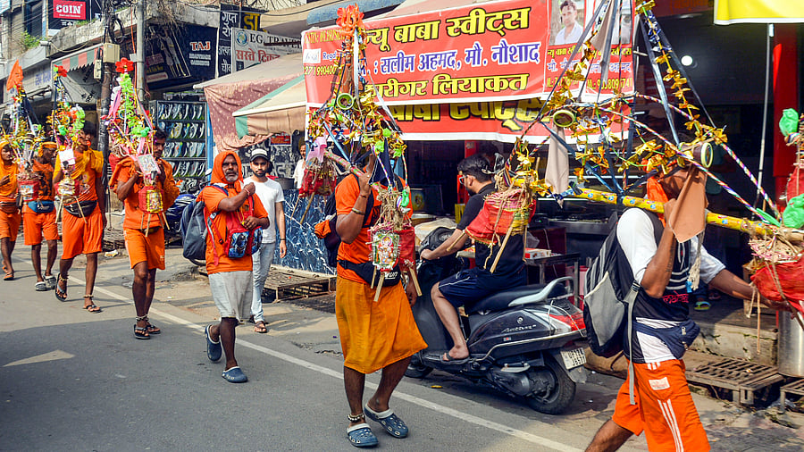 <div class="paragraphs"><p>Kanwariyas walk past the shops on which banners with shopkeepers' name were put up on Kanwar Marg after an order issued by Uttar Pradesh Government, in Muzaffarnagar, Saturday, July 20, 2024.</p></div>