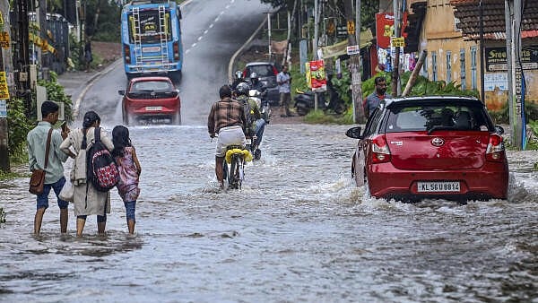 <div class="paragraphs"><p>Commuters make their way through a flooded road following rains in Kerala.&nbsp;</p></div>