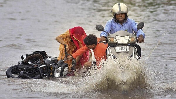 <div class="paragraphs"><p> Commuters on a two-wheeler lose balance on a waterlogged road after rain, in Bikaner.</p></div>