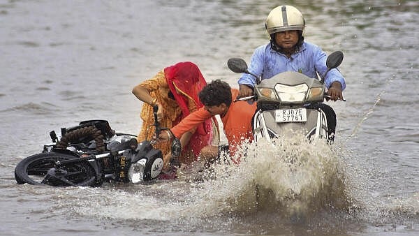 <div class="paragraphs"><p>Commuters on a two-wheeler lose balance on a waterlogged road after rain, in Bikaner. </p></div>